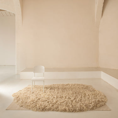 Beige deep shag rug on a light wooden floor with a white jean prouvé chair against a beige wall.