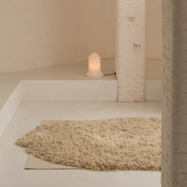 Candle on a white surface next to a textured rug in a minimalistic setting.