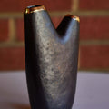 Black brass ase with gold accents on a white surface with a brick wall background