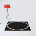Black rug with a circular design on a white floor, featuring a red lamp.
