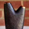 Dark brass vase with gold accents on a white surface with a brick wall background