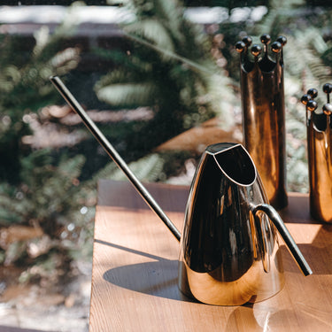Metallic watering can on a wooden surface with blurred greenery in the background