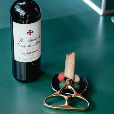 Red wine bottle with a corkscrew on a green surface