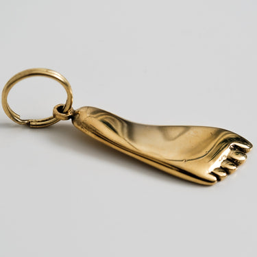 Gold foot-shaped keychain on a light gray background