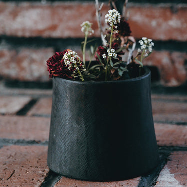 Black brass vase or pot with flowers on a brick surface