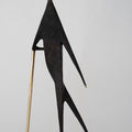 Abstract sculpture of a figure with a long neck and thin legs on a light gray background
