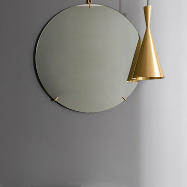 Round mirror with gold frame and pendant light on a gray wall in entryway