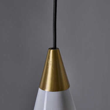 Close-up of a pendant light with a brass cone-shaped fixture against a gray background