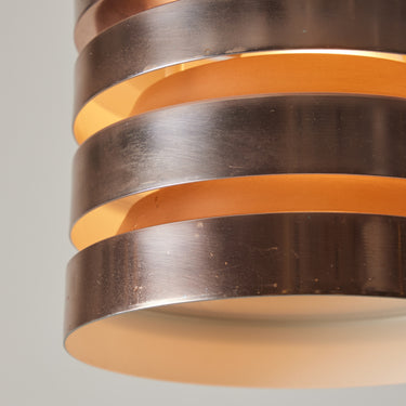 Close-up of a metallic cylindrical light pendant with concentric rings on a gray background