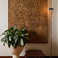Wooden wall art with a sunburst pattern in a room with a plant and decorative pillows.