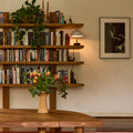 Dining room with wooden table, bookshelf, and colorful rug. Chapo B17 shelf in oak