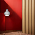 White cirque pendant light hanging against a red wall with a wooden floor and curtain.