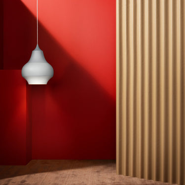 White cirque pendant light hanging against a red wall with a wooden floor and curtain.