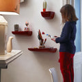 Person standing in a room with red wall shelves displaying various items.