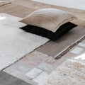 Close-up of a textured rug with floor cushion neutral pillows on a stone floor