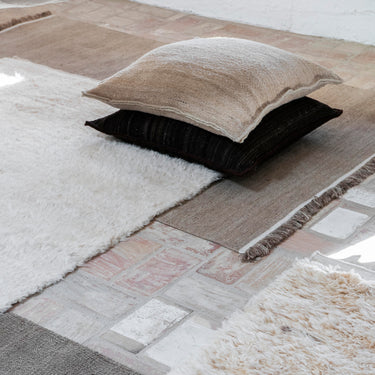 Close-up of a textured rug with floor cushion neutral pillows on a stone floor