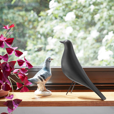Decorative vitra house bird in black ash and a purple plant on a windowsill with a blurred green outdoor background