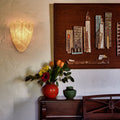 Decorative wall sconce, wooden panel with art pieces, and a vase with flowers on a wooden cabinet.