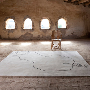Wooden chair on a large white rug in a room with arched windows and wooden beams.