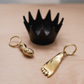 Two gold keychains shaped like feet and a black crown on a beige surface.
