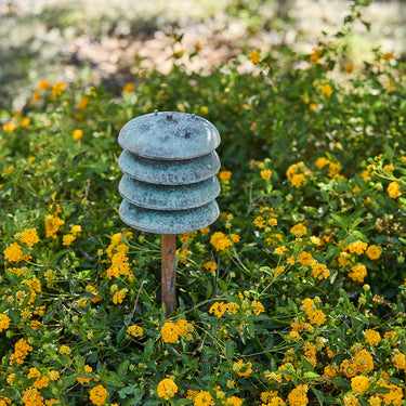 Decorative garden light with verdigris shade in a garden setting with yellow flowers.