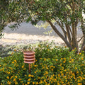 Decorative garden lighting in copper with layered design in a garden setting with flowers and trees.