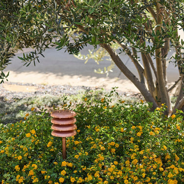 Decorative garden lighting in copper with layered design in a garden setting with flowers and trees.