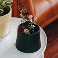 Black planter with flowers on a white table next to a brown leather couch.