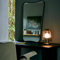 Modern interior with a gio ponti fa mirror mirror, lamp, and chair against a dark wall.