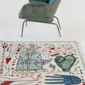 Decorative rug with abstract designs on a white floor with a chair.