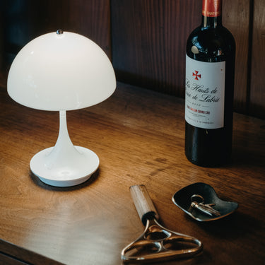 White lamp, bottle of red wine, and wine opener on a wooden surface.