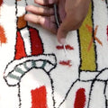 Close-up of a hand tufting on a colorful patterned rug with red, white, and yellow colors.
