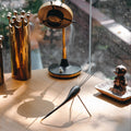 Collection of decorative items including a tall cylindrical object, a small round item, and a tall metallic object on a wooden surface.