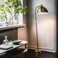 Gold floor lamp in a room with a window and plant