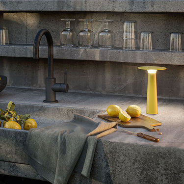 Modern kitchen sink area with black faucet, lemon, cutting board, and yellow lamp.