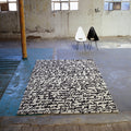 Black and white patterned rug on a concrete floor with two chairs in an industrial setting.