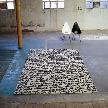 Black and white patterned rug on a concrete floor with two chairs in an industrial setting.