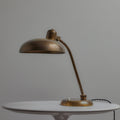 Bronze brass lariolux desk lamp on a white surface with a gray background