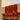 A terracotta red and dusty pink patterned textile, likely a rug or tapestry, hanging from a beige stucco building under a pale blue sky.