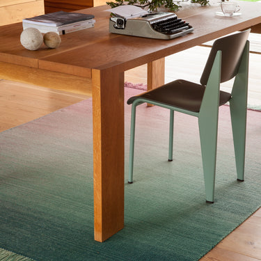 Wooden dining table with a typewriter and decorative items, jean prouve standard chair set on a green rug.