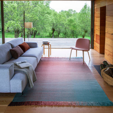 Modern living room with a gray sofa, colorful ombré  rug, and wooden floor.