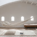Hammock in a minimalist room with white walls, wooden floor, and plants.
