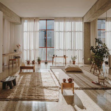 Modern living room with large windows, neutral decor, and a rug. Artek stools and cesta lamp included