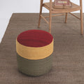 Multicolored ottoman on a brown carpet with a wooden chair in the background.