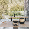 Modern outdoor furniture set with a table, chairs, and striped ottomans in a forest setting.