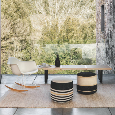 Modern outdoor furniture set with a table, chairs, and striped ottomans in a forest setting.