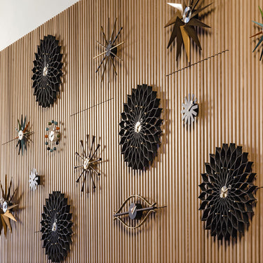 Decorative George Nelson for Vitra wall clocks with black and gold floral patterns on a wooden panel.
