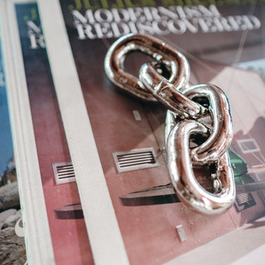 Silver chain link pendant on a magazine with a building in the background