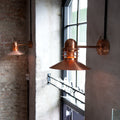 Two copper wall-mounted lamps on a textured wall with a window in the background.
