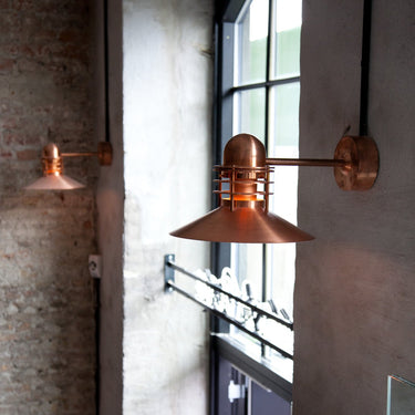 Two copper wall-mounted lamps on a textured wall with a window in the background.